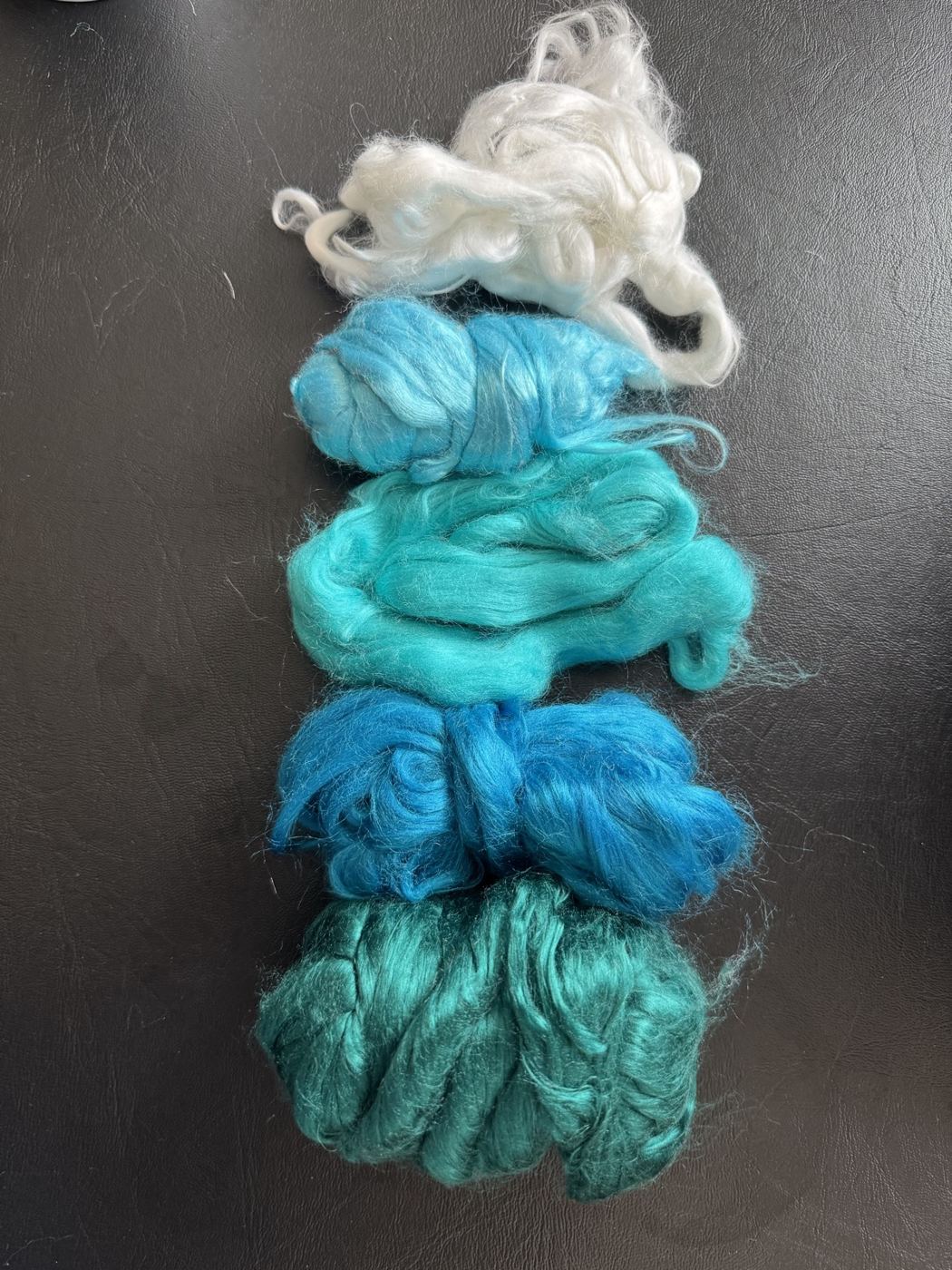 Teal, turquoise and white wool and silk fibres arranged as a colour palette